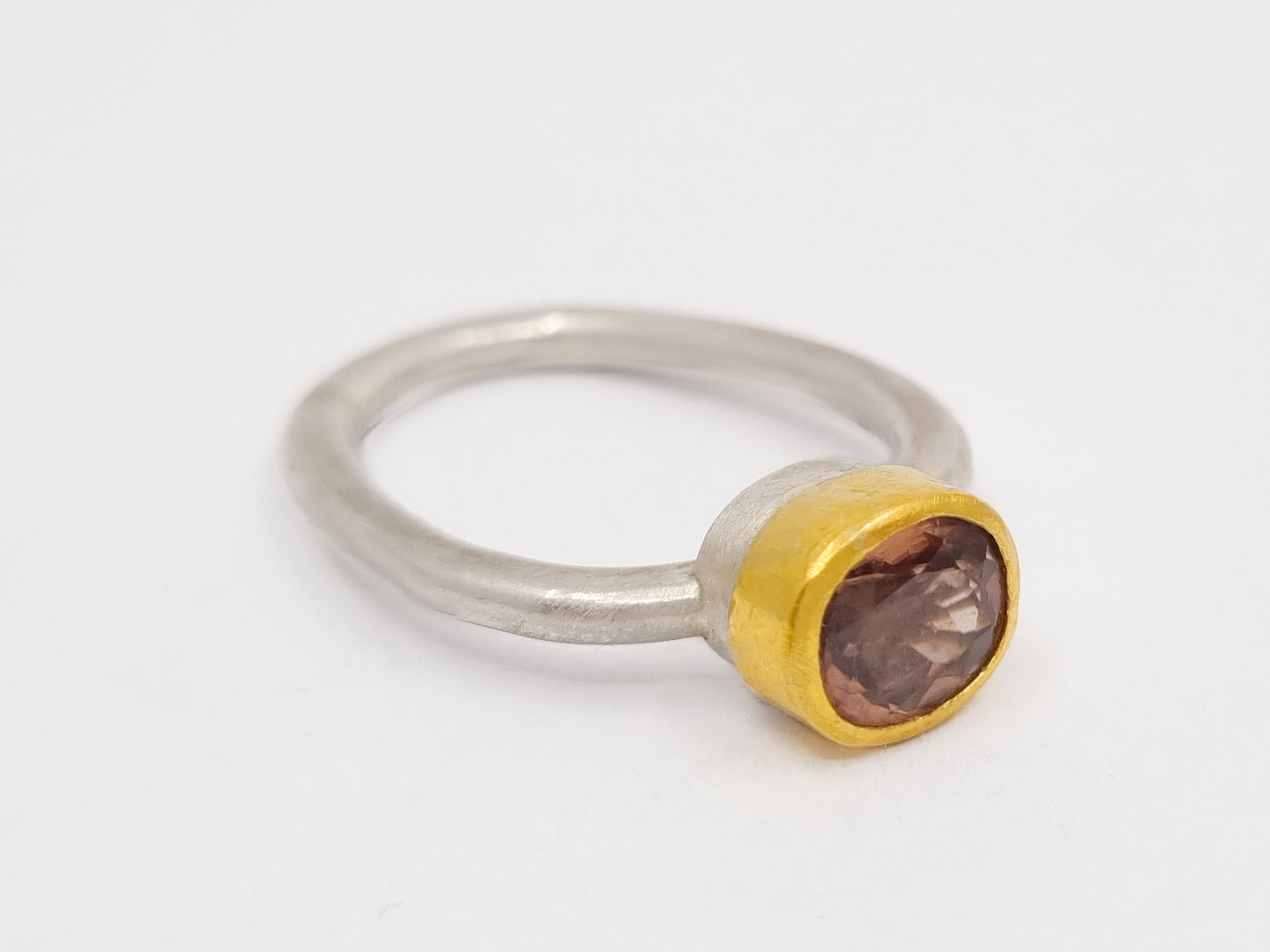 Handgeschmiedeter Ring aus mattem Silber mit 900er Goldfassung, die einen facettierten, champagnerfarbenen Spinell hält. Der Ring liegt auf hellem Hintergrund und zeigt die klare Form und den warmen Glanz des Steins.