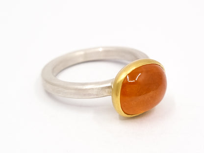 Silberner Ring in Größe 57 mit mattierter Oberfläche, der einen runden Mandarin-Granat-Cabochon in einer goldenen Fassung hält. Der Stein leuchtet in kräftigem Orange-Rot, der Kontrast zwischen kühlem Silber und warmem Gold ist deutlich zu sehen.