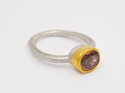 Handgeschmiedeter Ring aus mattem Silber mit 900er Goldfassung, die einen facettierten, champagnerfarbenen Spinell hält. Der Ring liegt auf hellem Hintergrund und zeigt die klare Form und den warmen Glanz des Steins.
